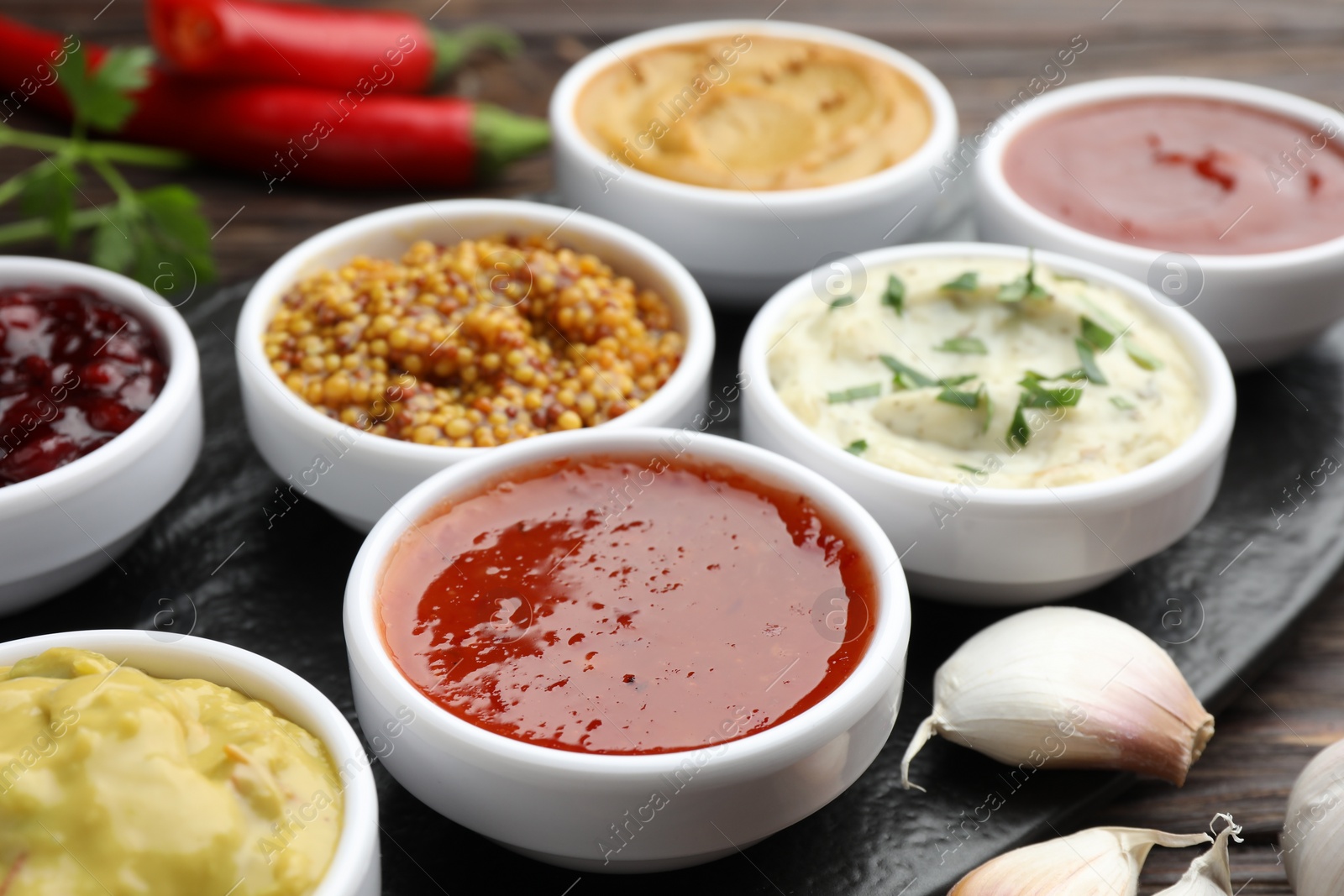 Photo of Different tasty sauces in bowls and garlic on table, closeup