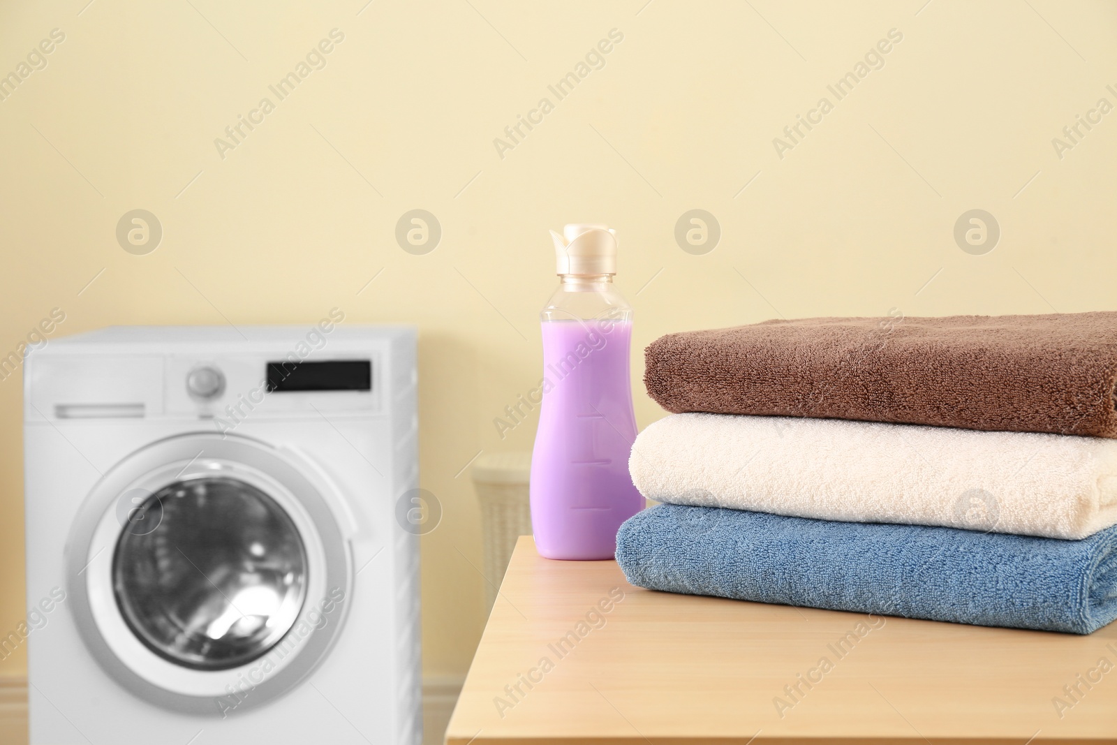 Photo of Clean towels and bottle of detergent on table in laundry room. Space for text