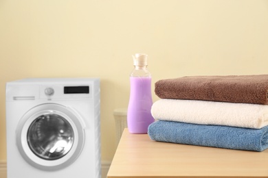 Photo of Clean towels and bottle of detergent on table in laundry room. Space for text