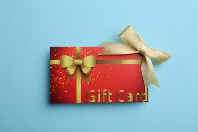 Photo of Gift card with bow on light blue background, top view