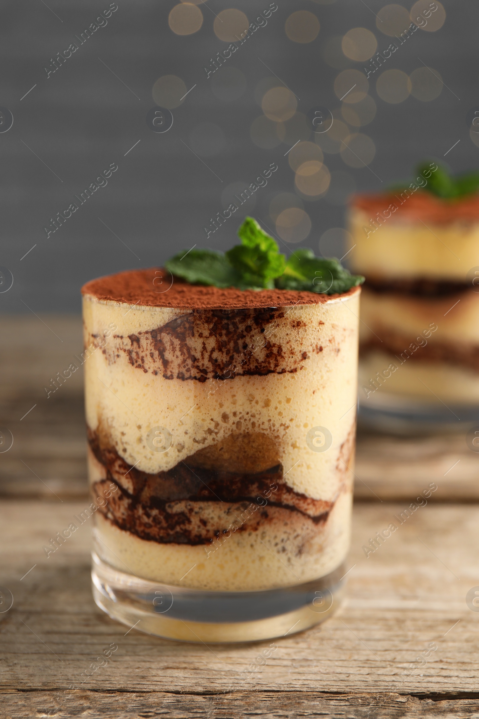 Photo of Tasty tiramisu and mint in glasses on wooden table, closeup