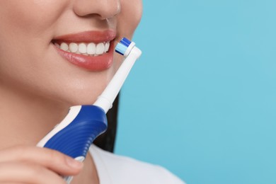 Photo of Woman brushing her teeth with electric toothbrush on light blue background, closeup. Space for text