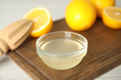Photo of Freshly squeezed lemon juice in bowl on wooden board, closeup