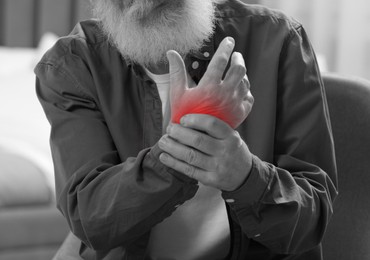 Senior man suffering from pain in wrist indoors, closeup. Black and white effect