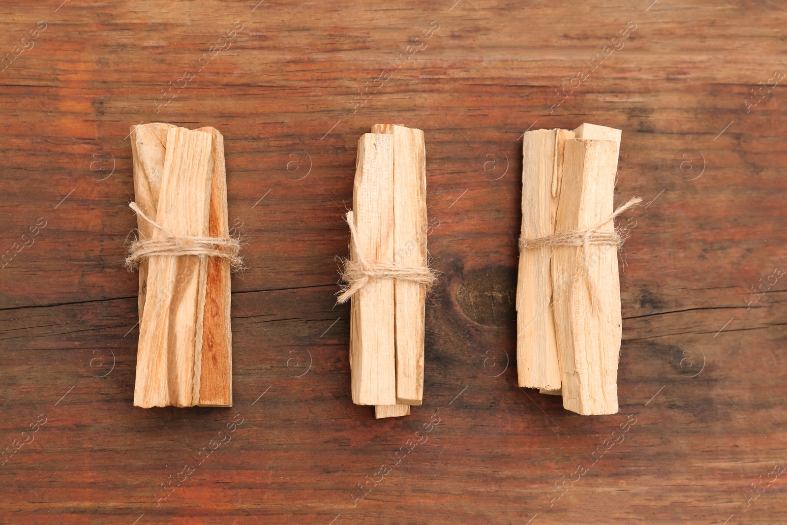 Photo of Bunches of tied Palo Santo sticks on wooden table, flat lay