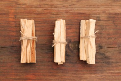 Photo of Bunches of tied Palo Santo sticks on wooden table, flat lay