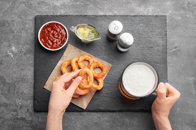 Woman eating fried onion rings with sauce at table, top view