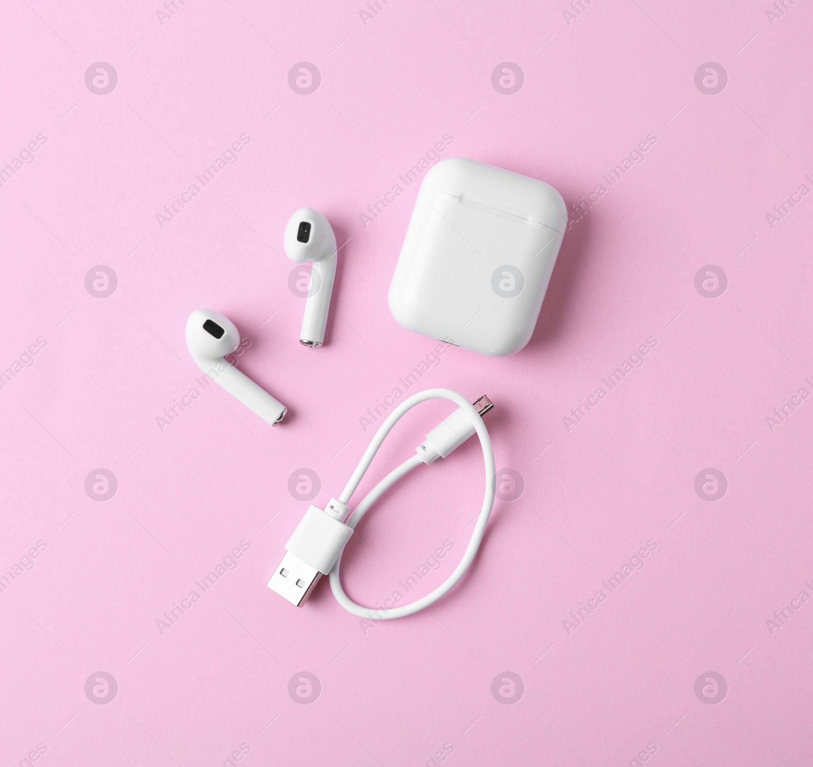 Photo of Modern wireless earphones and charging case with cable on pink background, flat lay