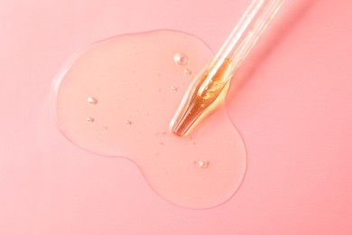 Photo of Dripping hydrophilic oil from pipette on pink background, top view