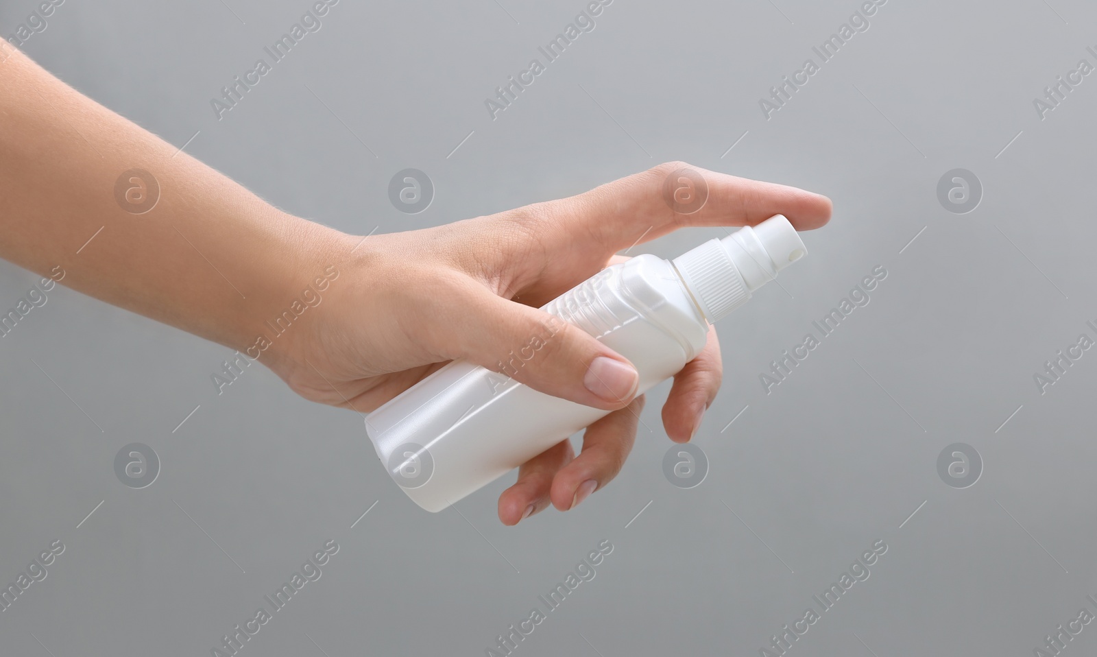 Photo of Woman with bottle of insect repellent spray on grey background, closeup
