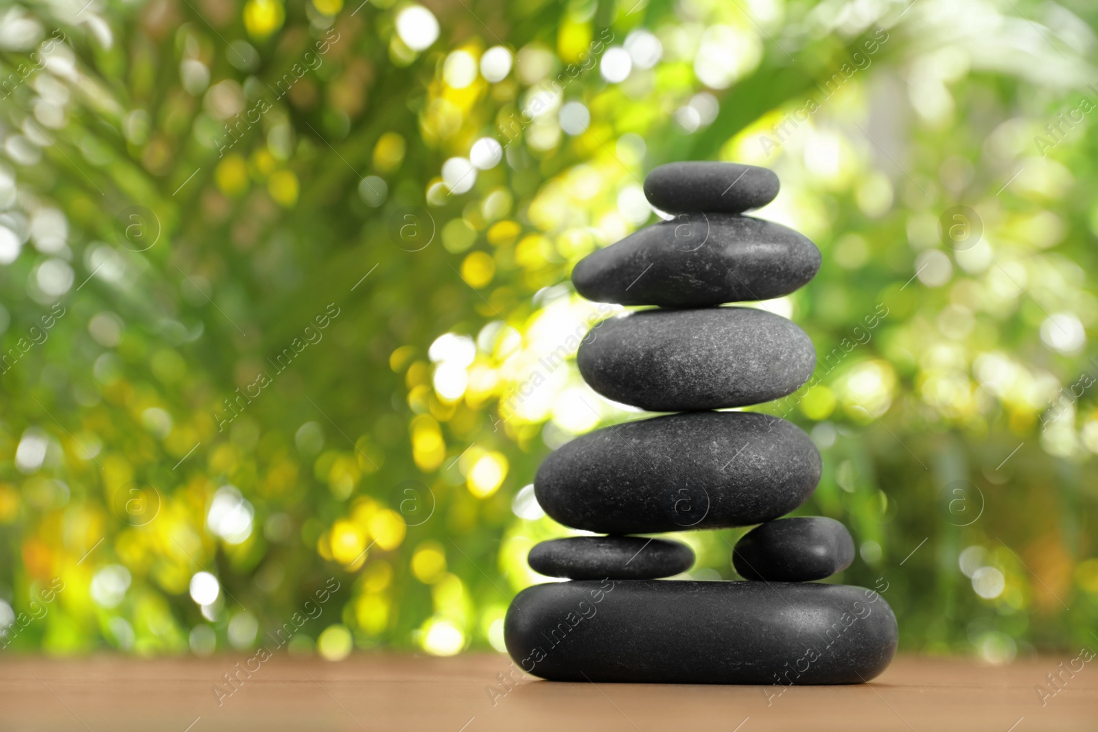 Photo of Table with stack of stones and blurred green leaves on background, space for text. Zen concept