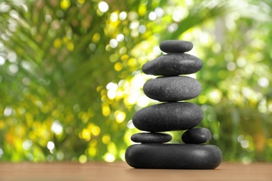 Photo of Table with stack of stones and blurred green leaves on background, space for text. Zen concept