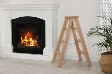 Wooden folding ladder near fireplace and potted plant in room