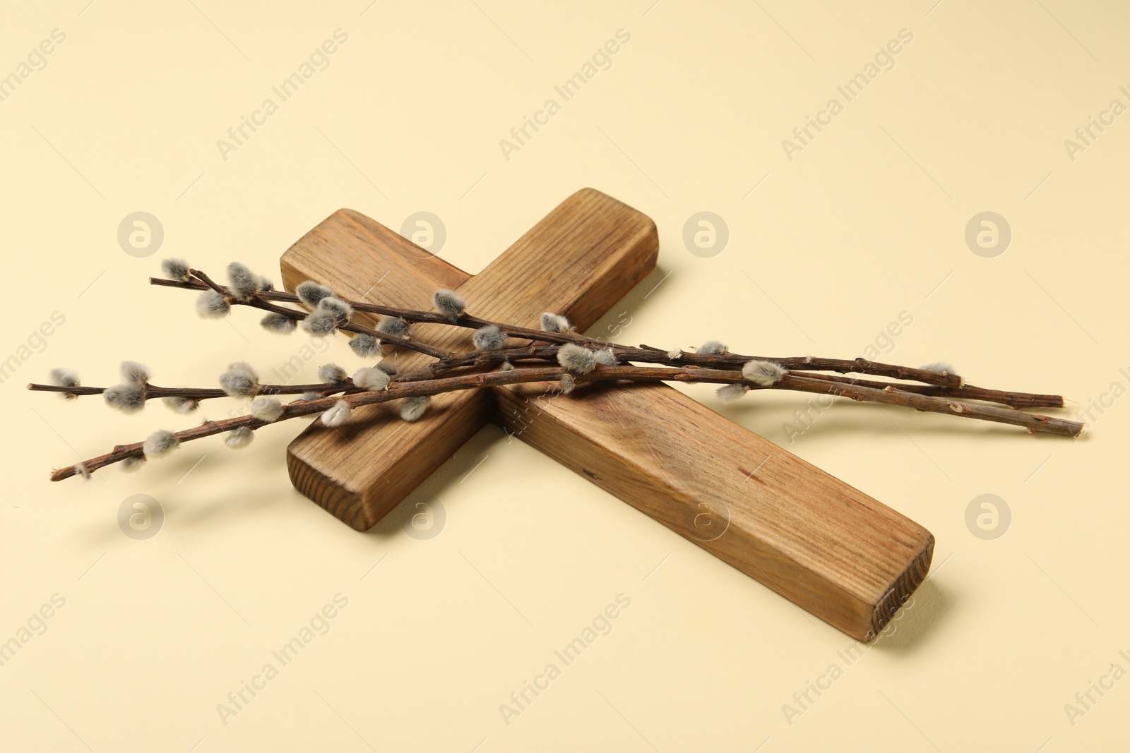 Photo of Wooden cross and willow branches on beige background. Easter attributes