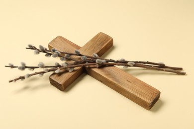 Photo of Wooden cross and willow branches on beige background. Easter attributes