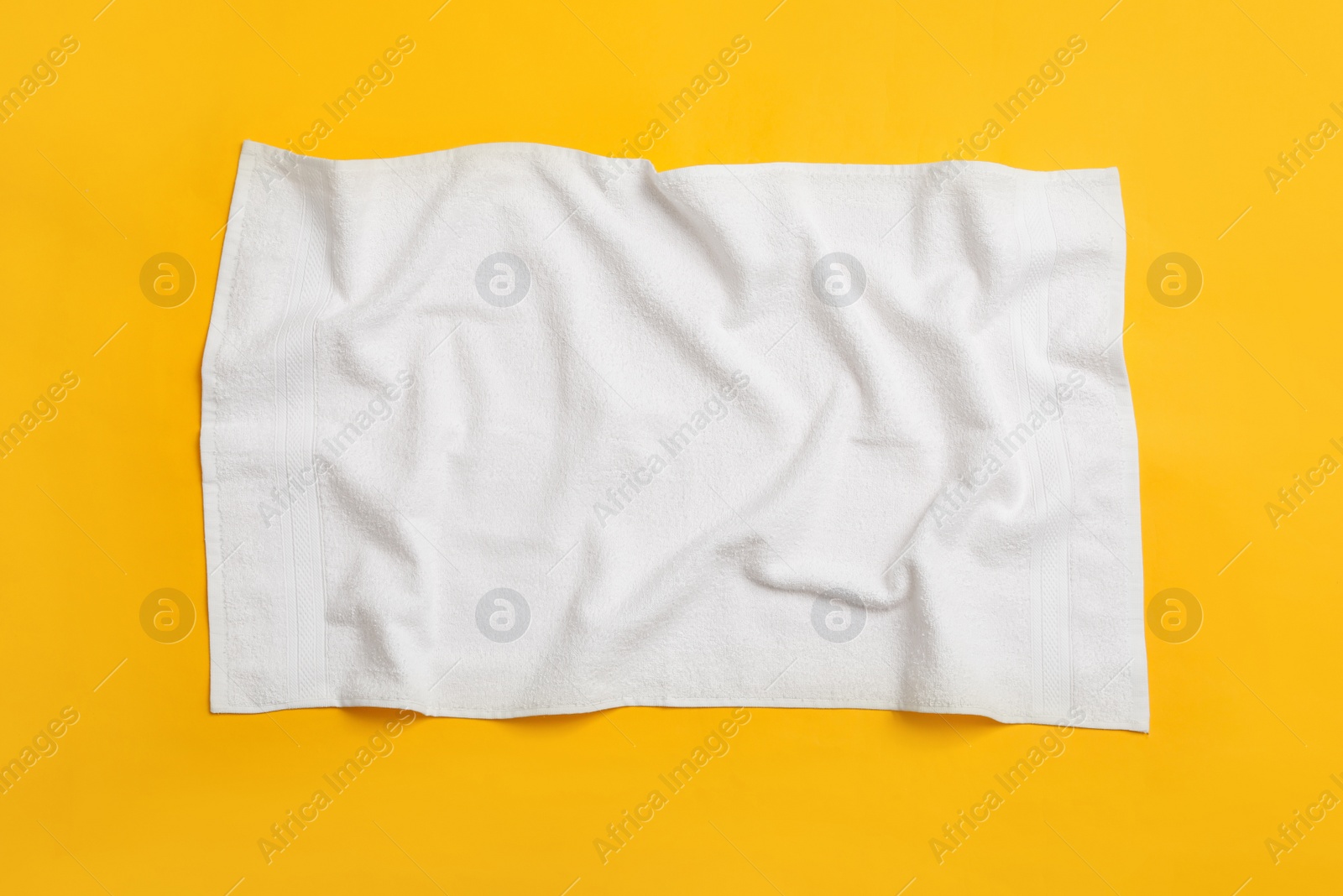 Photo of Crumpled white beach towel on yellow background, top view