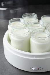 Photo of Modern yogurt maker with full jars on grey table