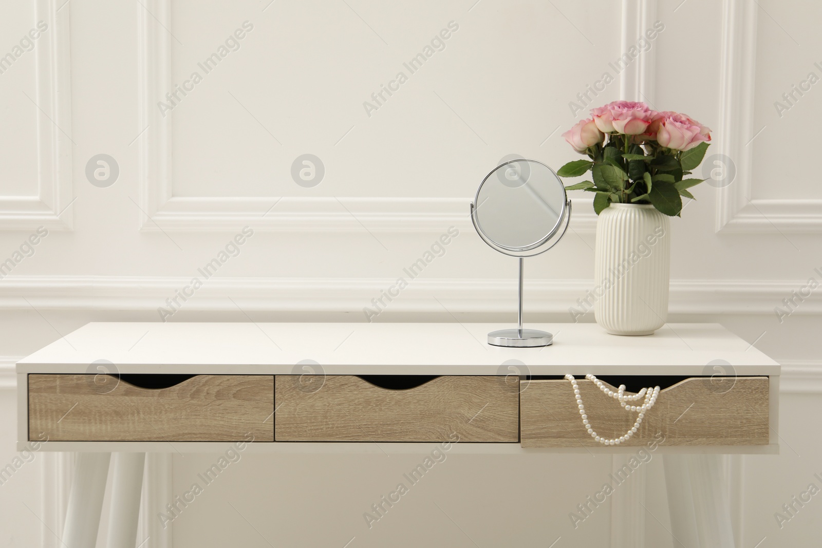 Photo of Mirror and vase with pink roses on white dressing table in makeup room, space for text