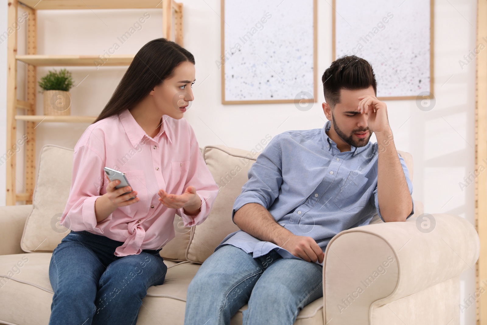 Photo of Young couple arguing about smartphone at home. Problems in relationship