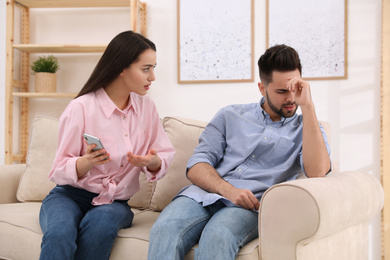 Photo of Young couple arguing about smartphone at home. Problems in relationship