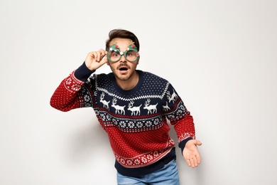 Young man in Christmas sweater with party glasses on white background