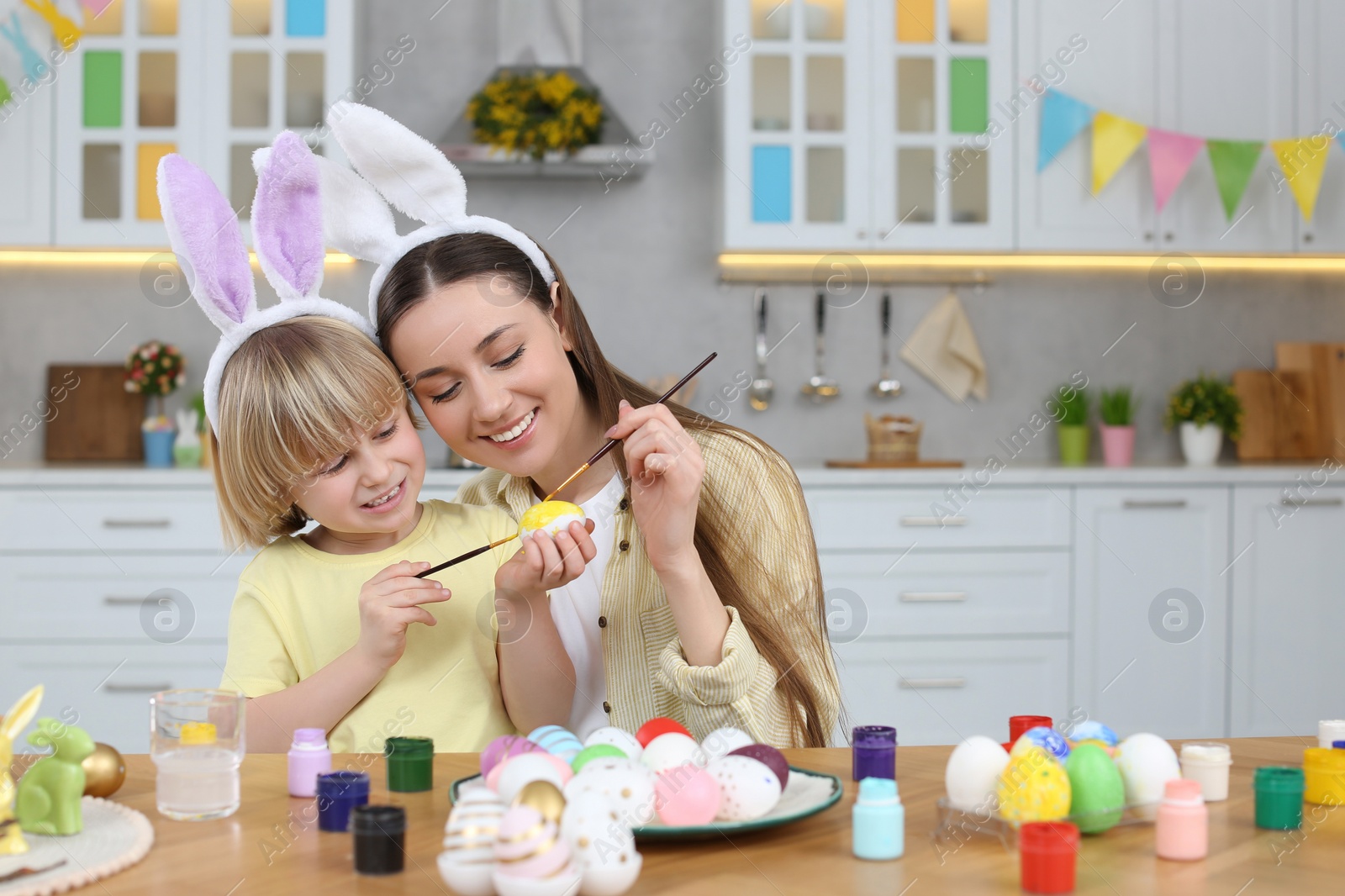 Photo of Mother and her cute son painting Easter eggs at table in kitchen