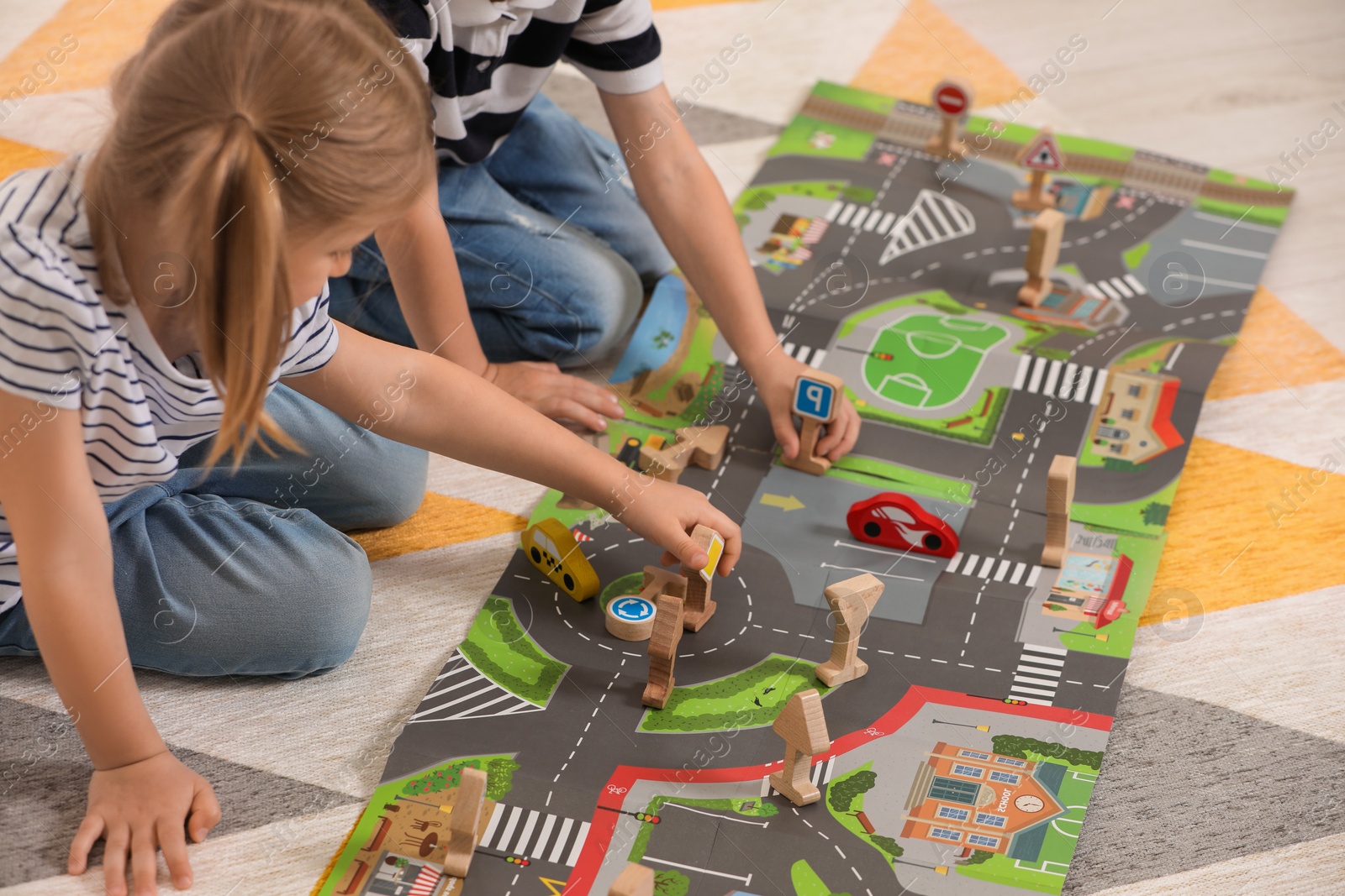 Photo of Little children playing with set of wooden road signs and toy cars indoors