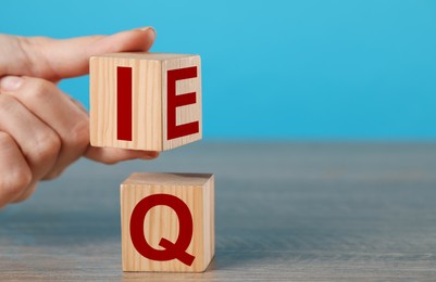 Photo of Woman turning cube with letters E and I above Q at wooden table, closeup. Space for text