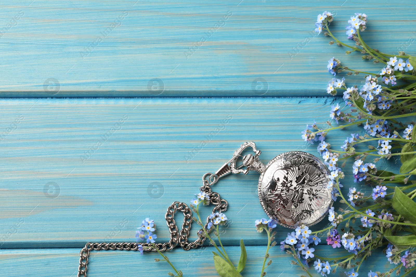 Photo of Beautiful Forget-me-not flowers and pocket watch on light blue wooden table, flat lay. Space for text