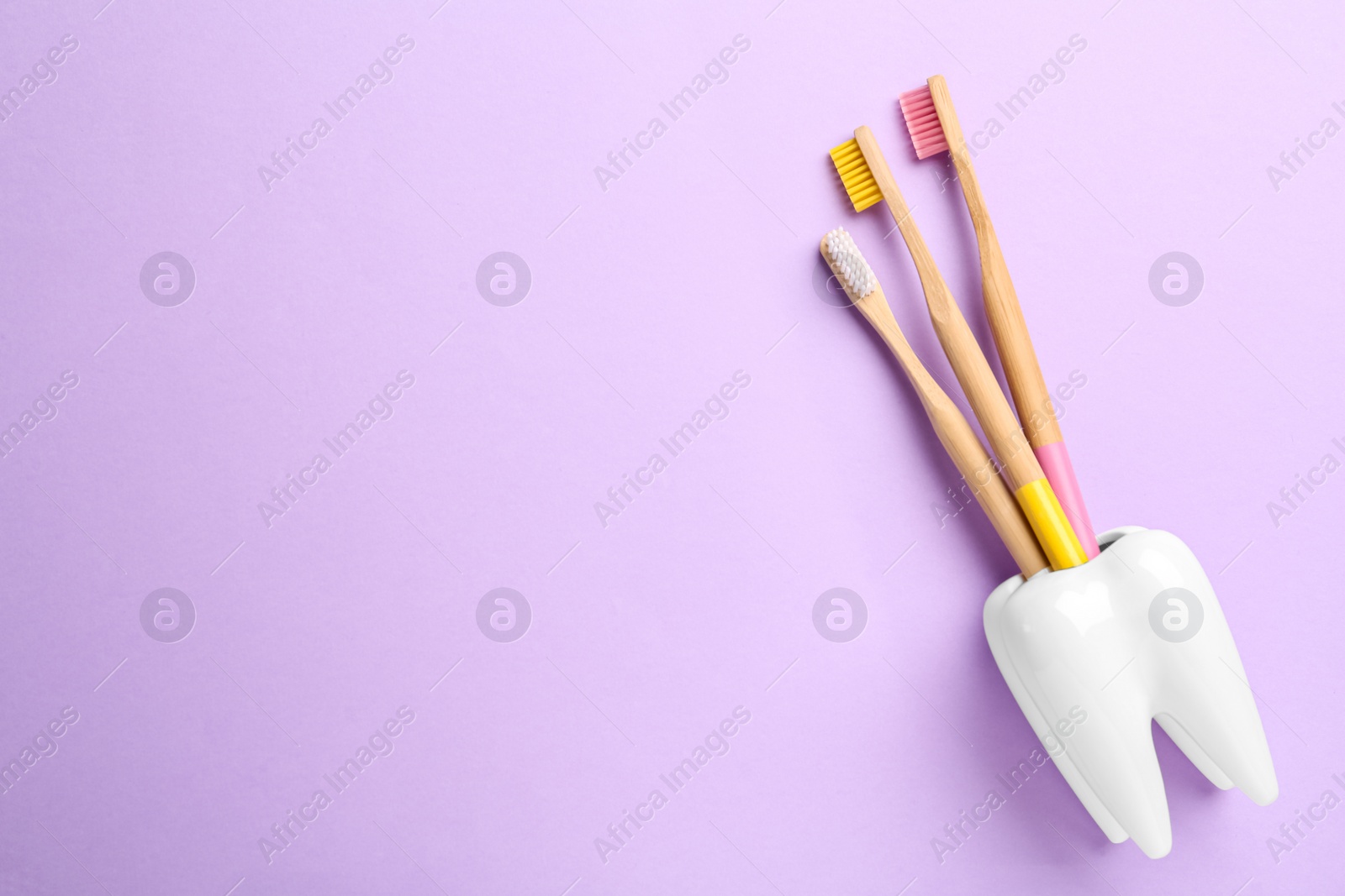 Photo of Wooden toothbrushes in holder on violet background, top view. Space for text
