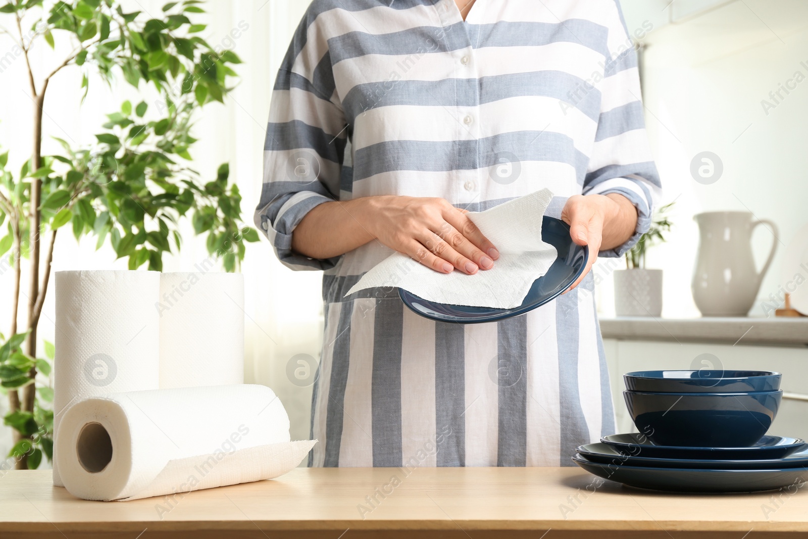 Photo of Woman wiping ceramic plate with paper towel indoors, closeup