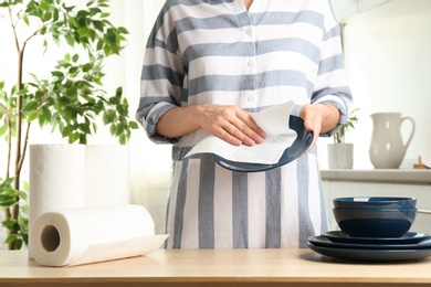 Woman wiping ceramic plate with paper towel indoors, closeup