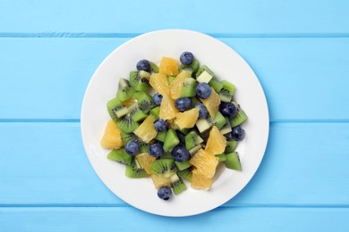 Photo of Plate of tasty fruit salad on light blue wooden table, top view