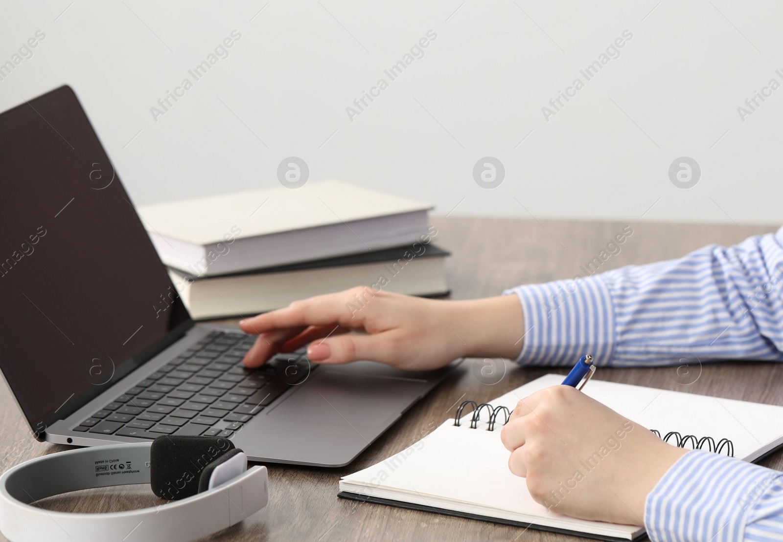 Photo of E-learning. Woman taking notes during online lesson at table indoors, closeup