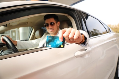 Photo of Man sitting in car and showing credit card at gas station, focus on hand