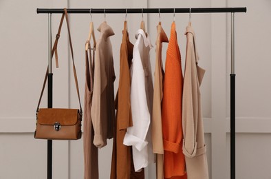 Rack with stylish women's clothes and bag near light wall