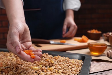 Photo of Making granola. Woman with dry apricots at table in kitchen, closeup