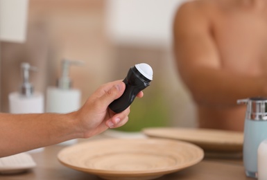 Photo of Young man holding deodorant in bathroom, closeup