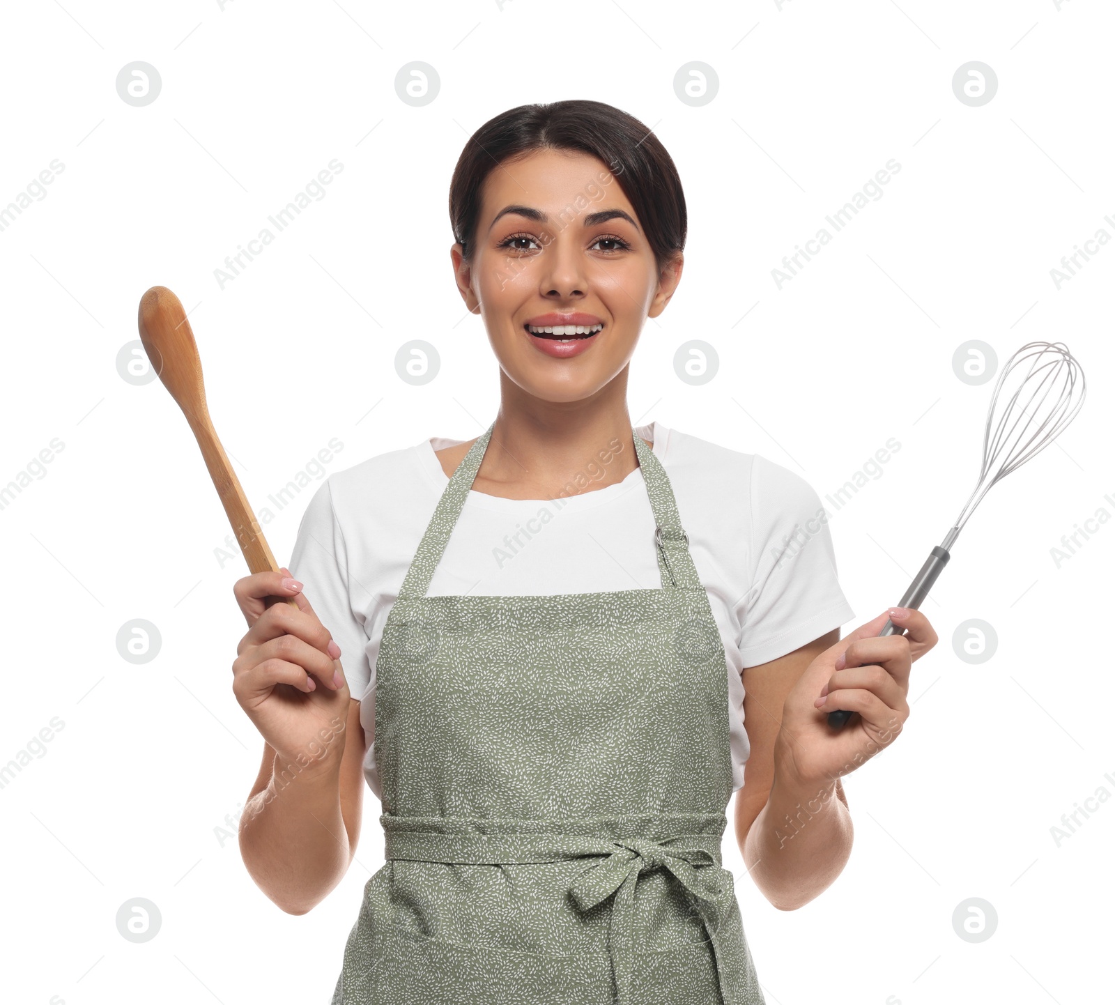 Photo of Young woman in green apron holding wooden spoon and whisk on white background