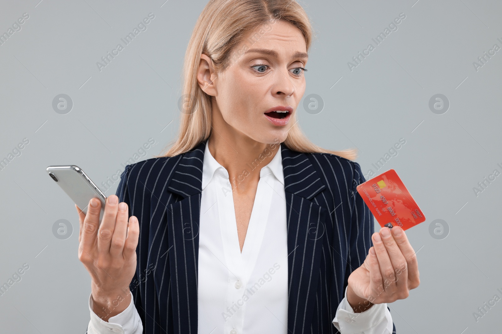 Photo of Stressed woman with credit card and smartphone on grey background. Be careful - fraud