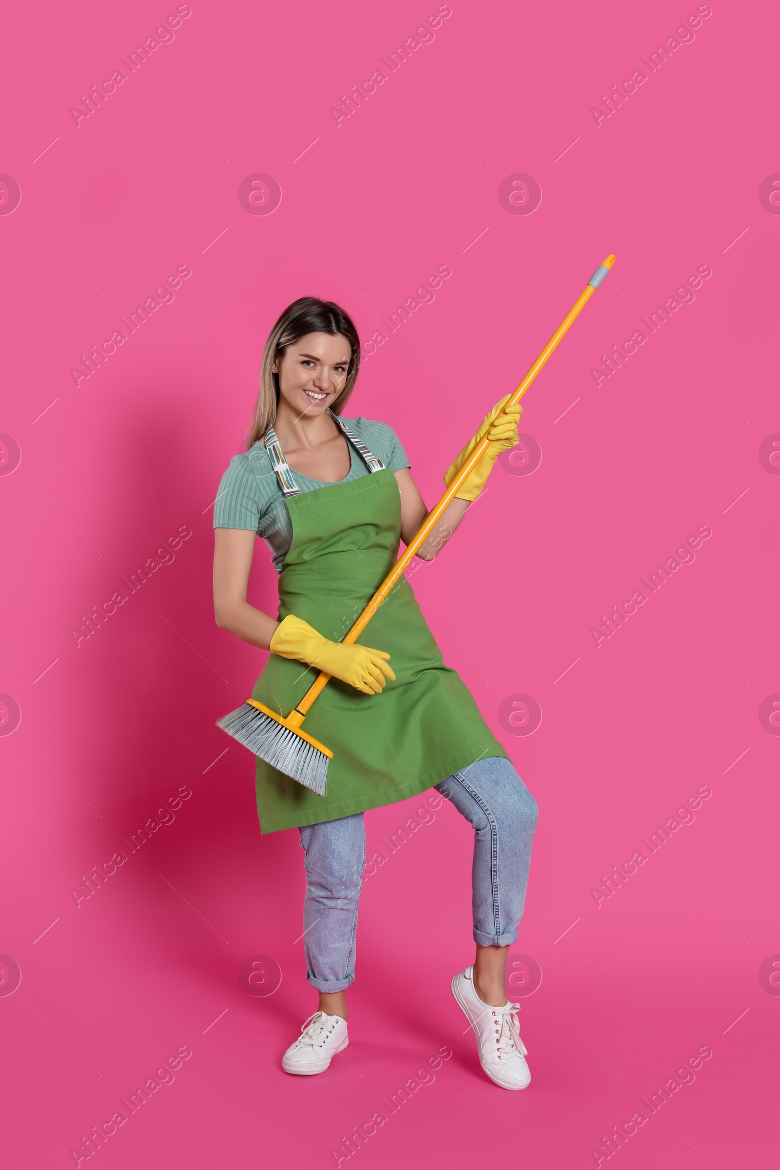 Photo of Young woman with yellow broom on pink background