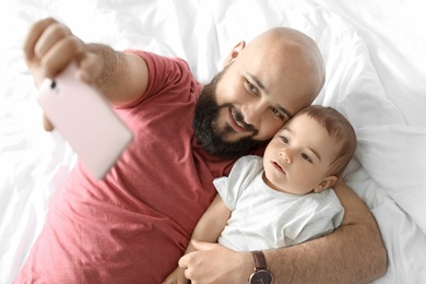 Photo of Dad taking selfie with his little son on bed