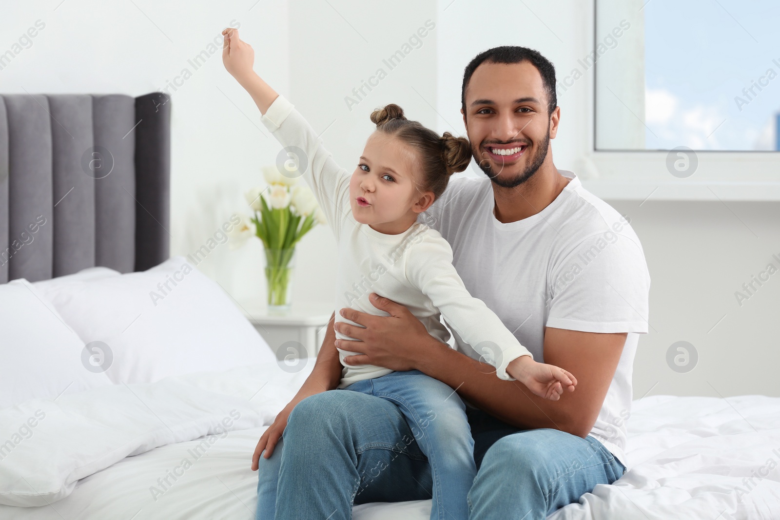 Photo of Little girl with her father spending time together on bed at home. International family