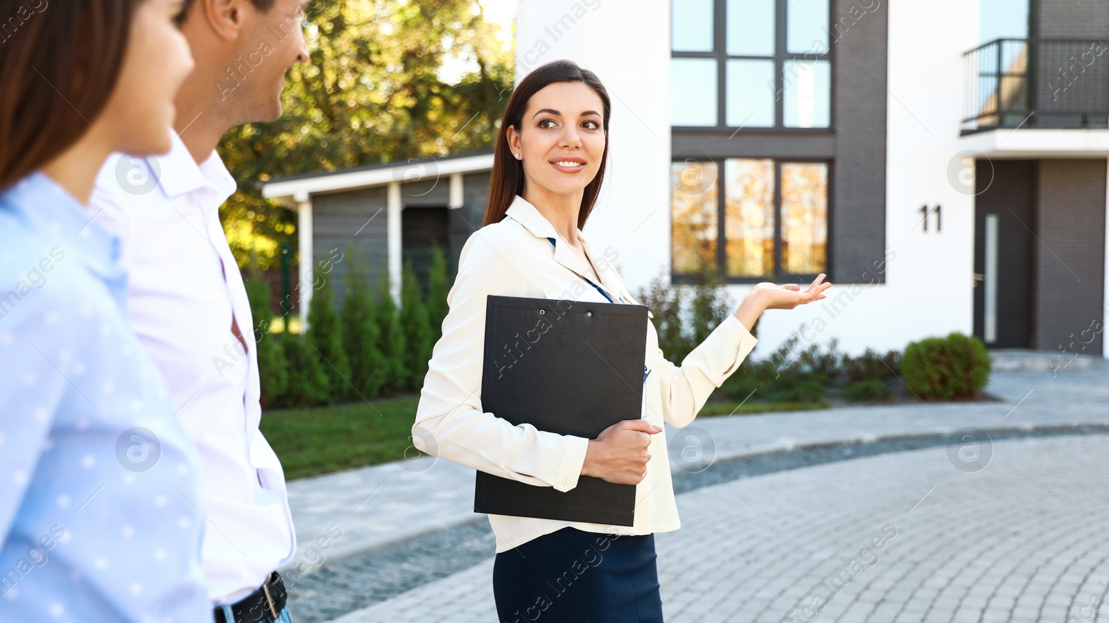 Photo of Real estate agent showing house to young couple outdoors