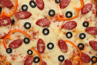 Tasty pizza with cheese, dry smoked sausages, olives and pepper as background, top view