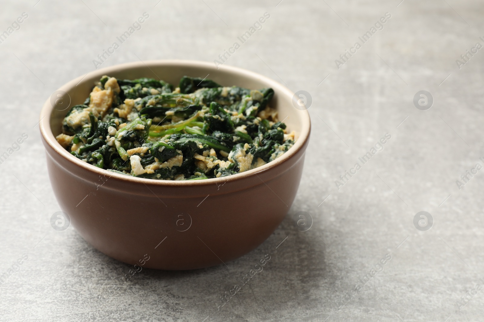 Photo of Tasty spinach dip with egg in bowl on grey table, closeup. Space for text