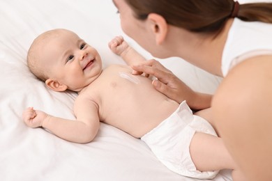 Photo of Woman applying body cream onto baby`s skin on bed, closeup