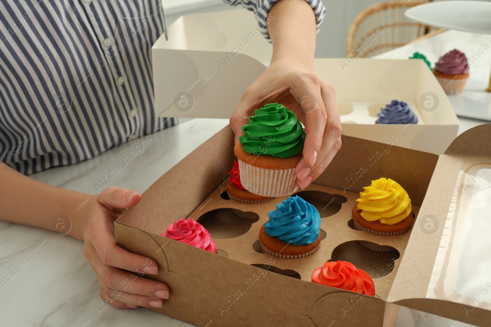 Photo of Woman with box of delicious colorful cupcakes at white marble table indoors, closeup