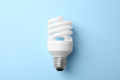 New modern lamp bulb on light blue background, top view