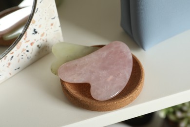 Photo of Jade and rose quartz gua sha tools on white shelf, closeup